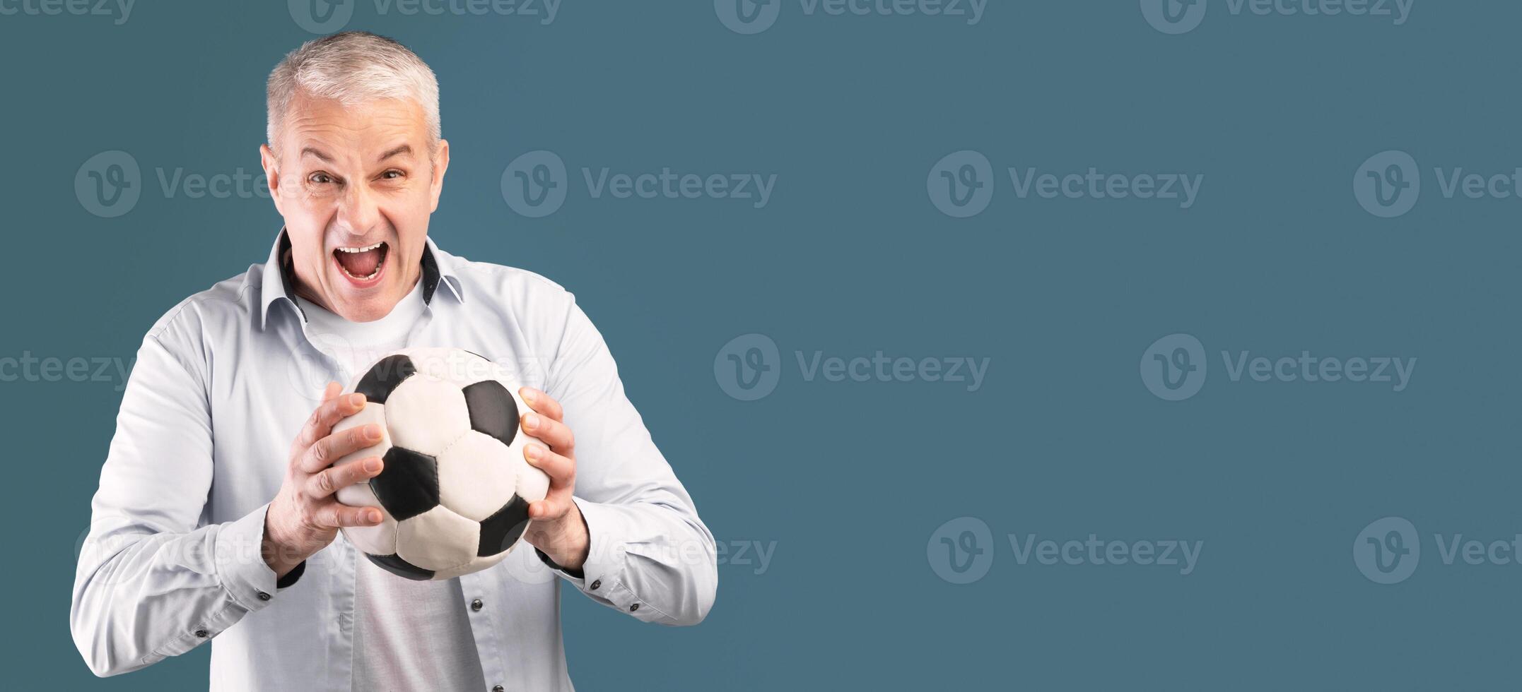 Mature Football Player. Excited cheering middle aged man posing with soccer ball on blue studio wall, panorama with copyspace photo