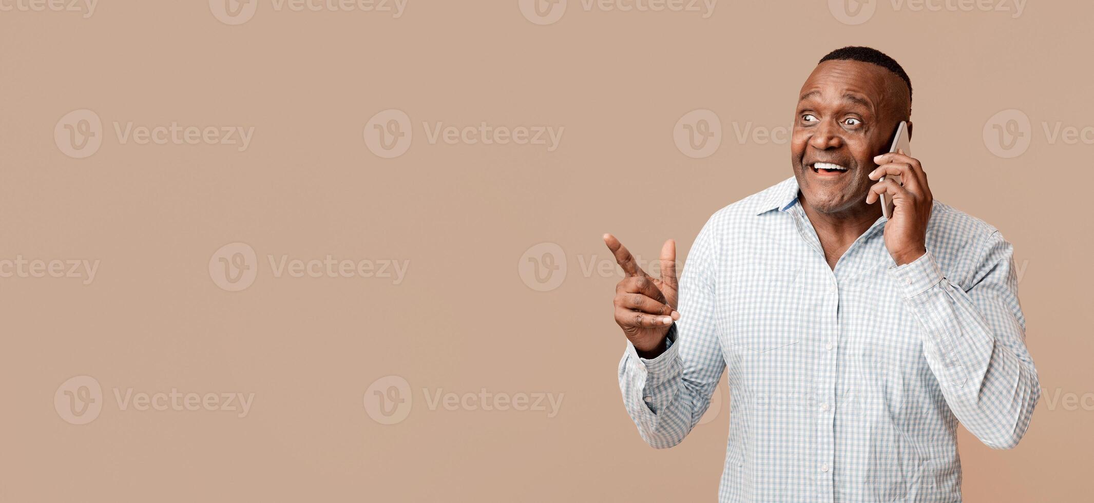 Roaming communication. Happy mature african man talking on cellphone, pointing at free space, orange studio background photo