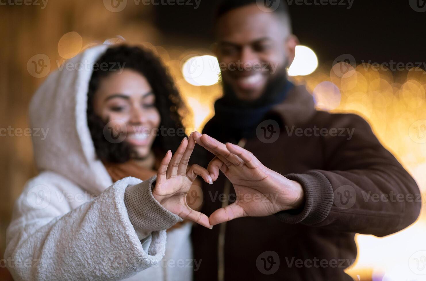 I Love You. Closeup of cheerful positive african american couple making heart shape with fingers walking together in the evening, looking at hands, selective focus, blurred background. Valentine's day photo