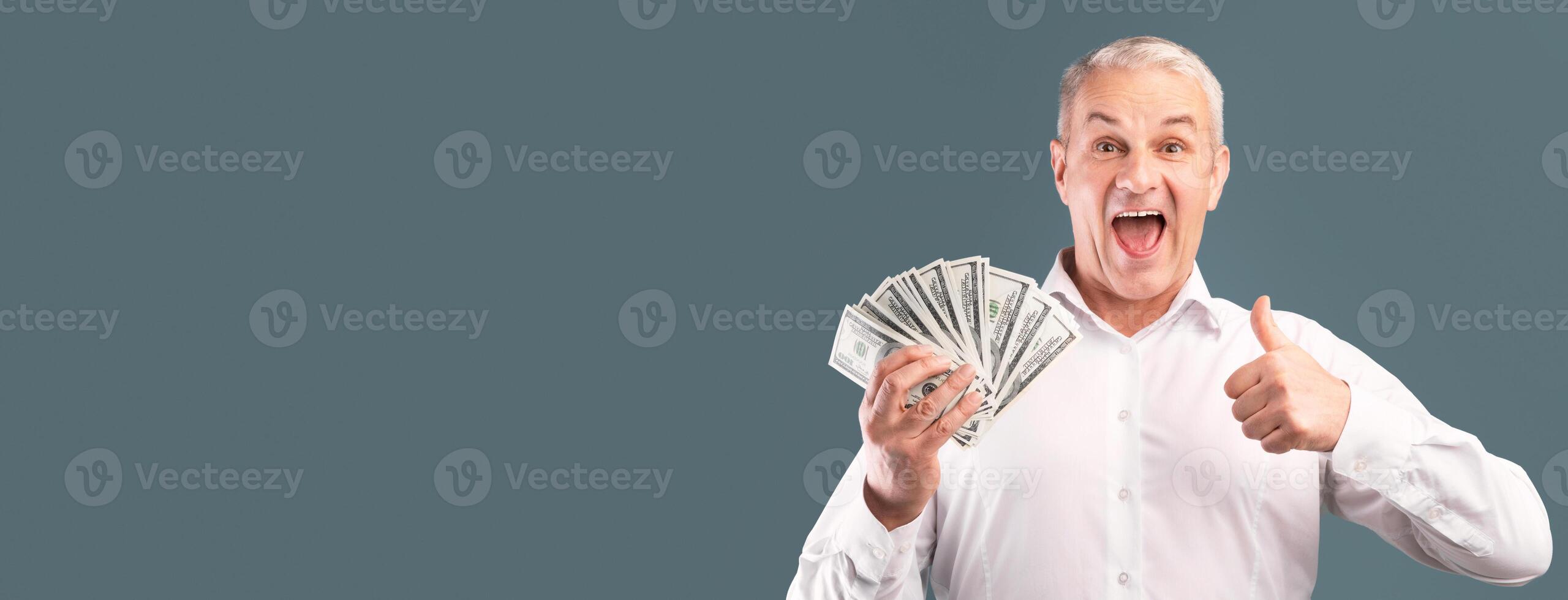 Money Saving Concept. Happy Senior Man Holding Money And Showing Thumbs Up Over Blue Studio Wall, Free Space photo