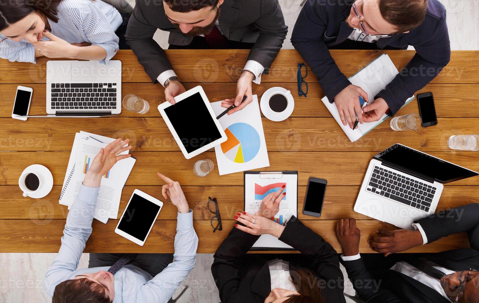 Business meeting top view. Busy people work in office, above view of wooden table with mobile phones, laptop, tablet and documents papers with diagram. photo