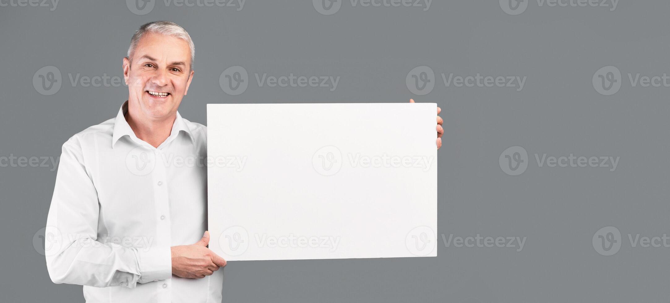 Happy Mature Man Showing Blank Placard With Copy Space For Your Text Isolated Over Gray Studio Wall photo