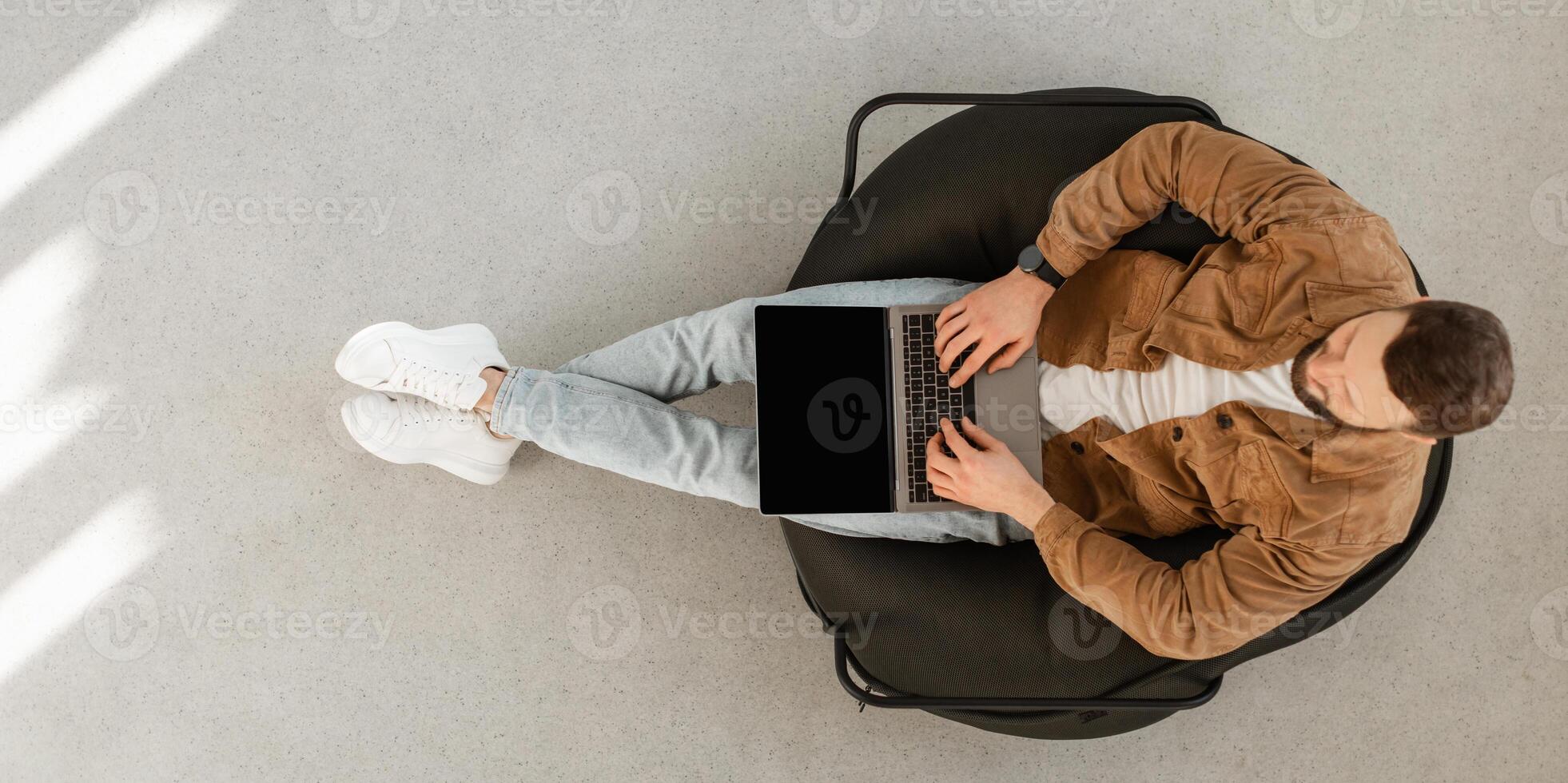 Male Freelancer Using Laptop Computer With Blank Screen Sitting In Chair At Home. Technology And Gadgets, Freelance Career And Lifestyle Concept. Top View Shot, Panorama, Mockup photo