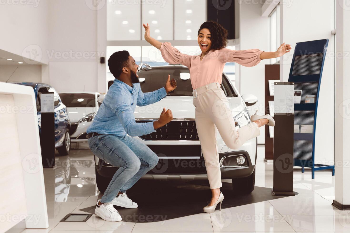 New Car Owners. Joyful African Couple Jumping Celebrating Buying Automobile In Dealership Showroom photo