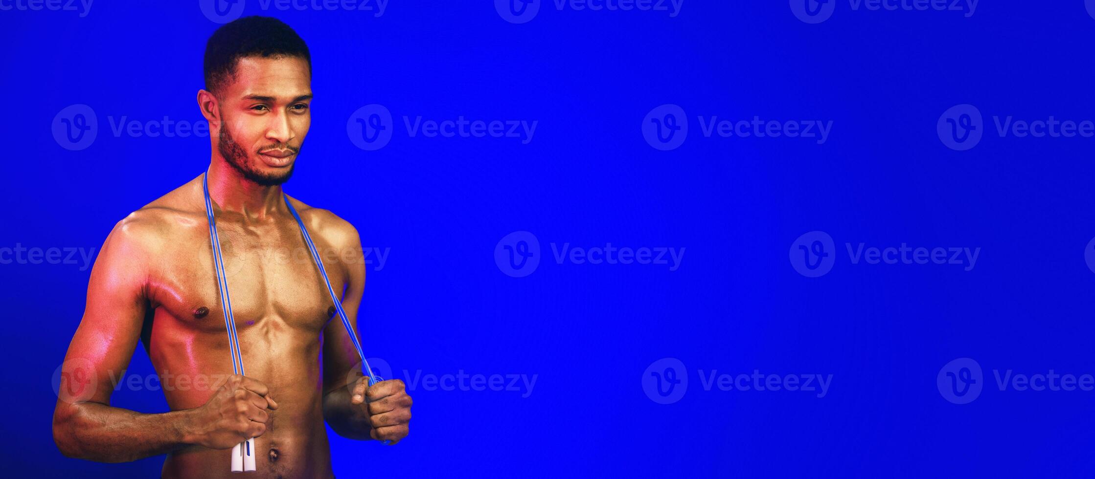 Fitness Concept. Athletic Black Man Holding Jumping Rope Posing On Blue Studio Background. Copy Space photo