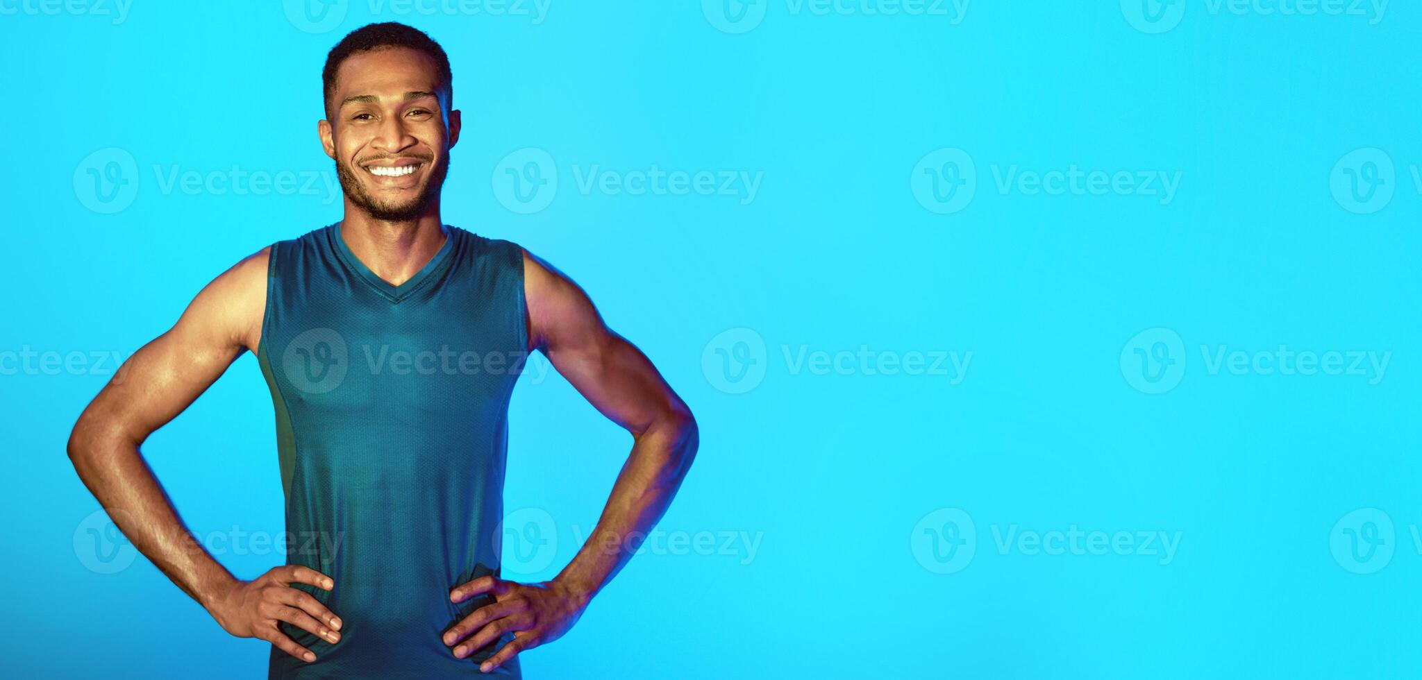Fitness Trainer. African Man In Sportswear Smiling To Camera Posing Standing Over Blue Background. Studio Shot, Neon Lights photo