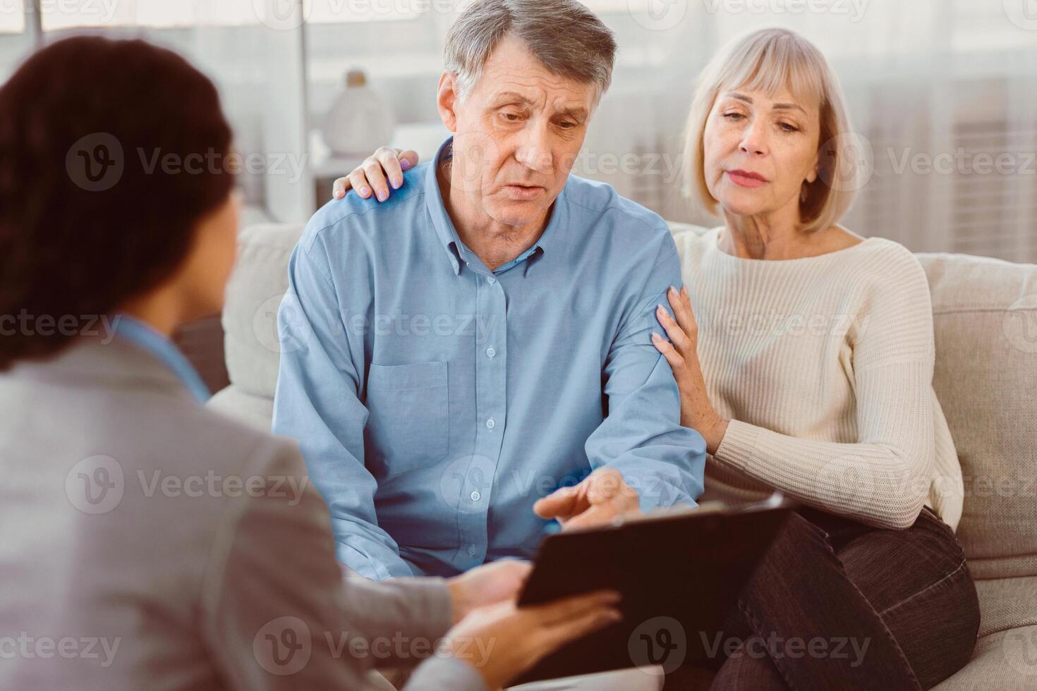 Last Will And Testament. Senior man sitting on couch with wife, checking document, signing papers with consultant photo