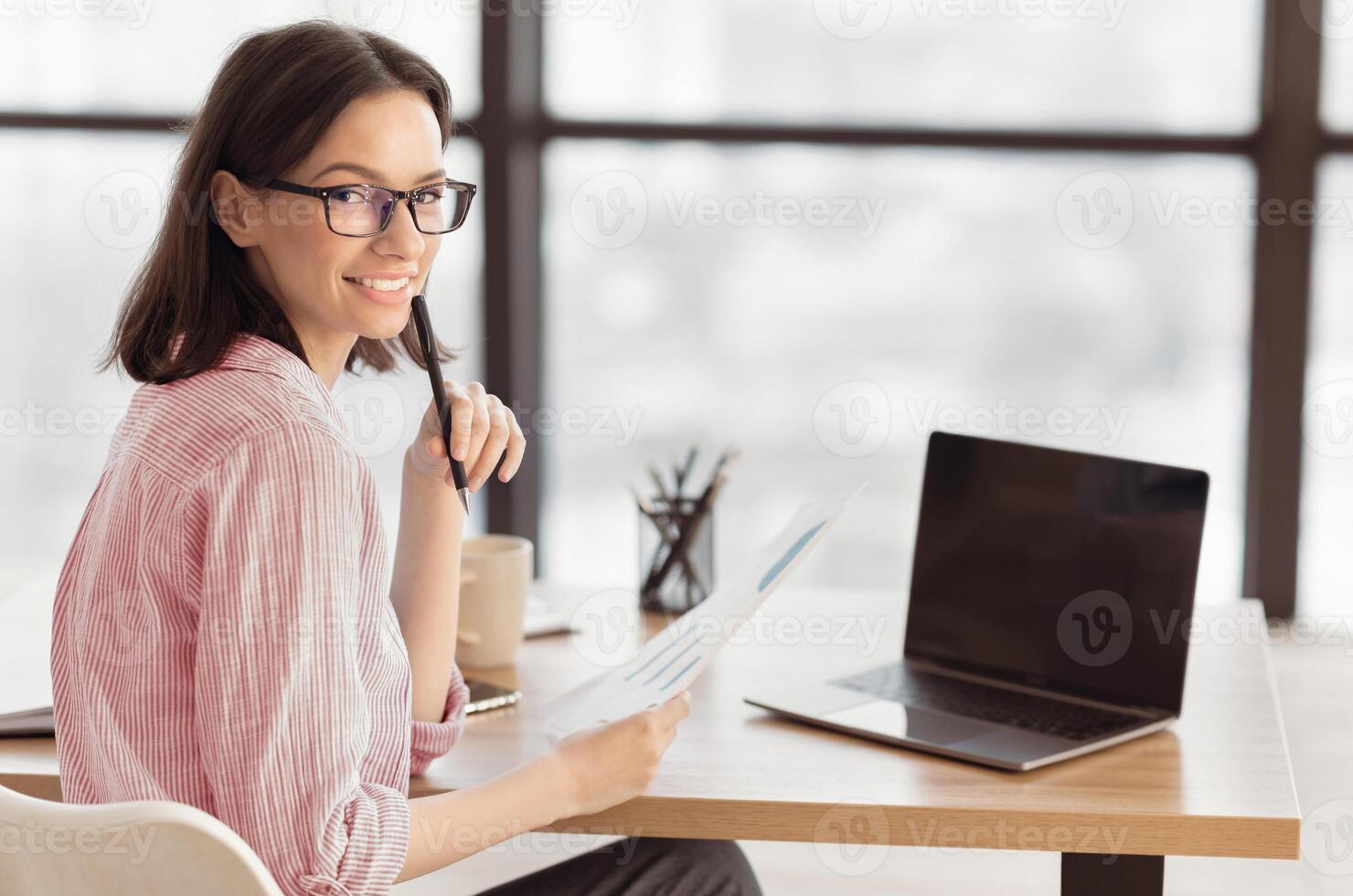 Over the Shoulder. Female Analyst Holding Paper With Statistics, Graphs and Charts Sitting at Desk in Creative Office photo