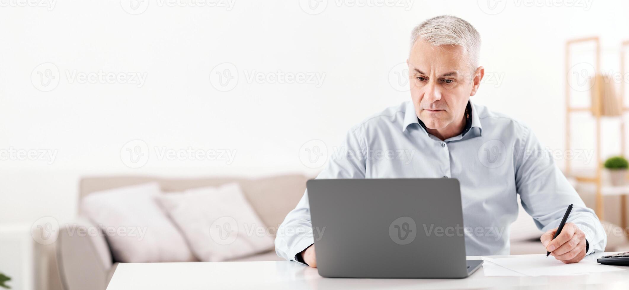 Note Taking. Attentive mature man writing details on paper and working on laptop, copyspace photo
