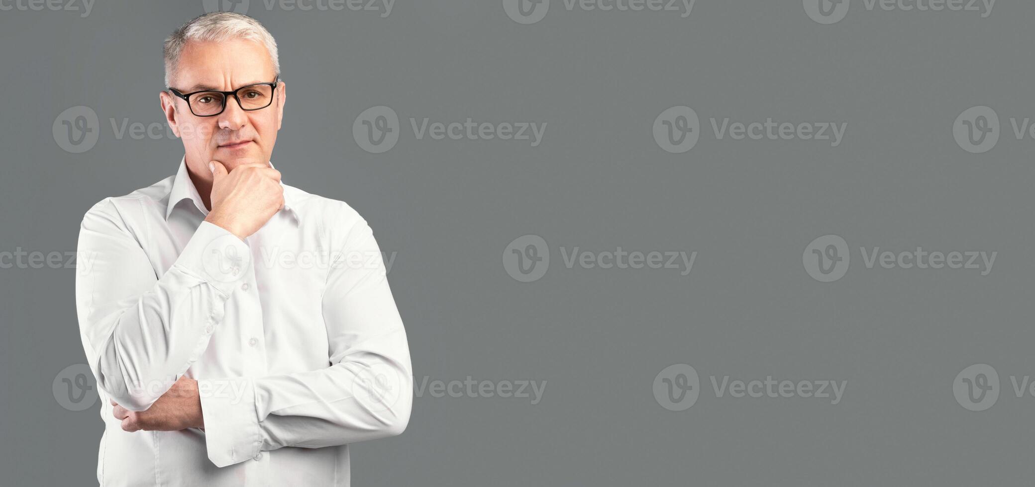 Making Decision. Portrait of pensive mature man in glasses looking at camera isolated over gray studio wall photo