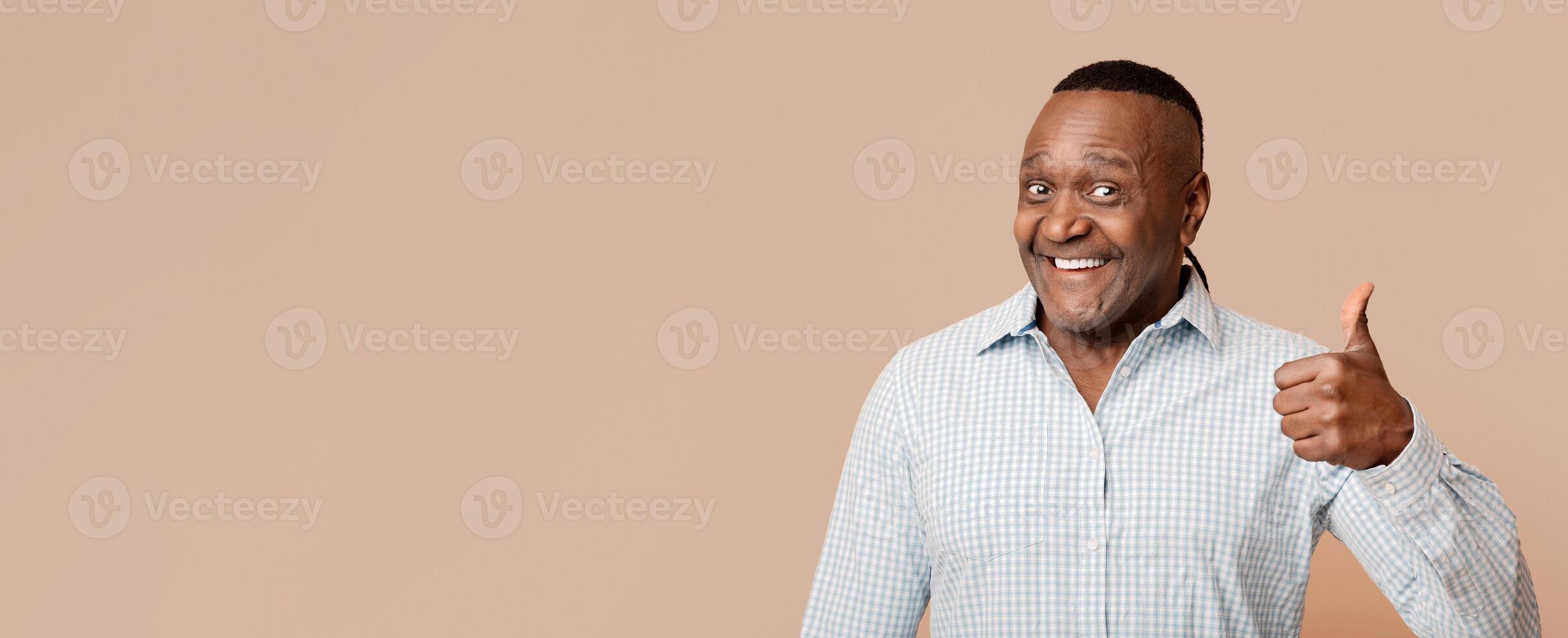 Happy middle aged african man gesturing thumb up, orange studio background photo