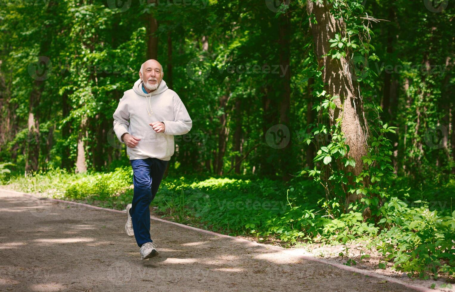 Elderly sporty man running in green forest during morning workout, copy space. Healthy and active lifestyle at any age concept photo