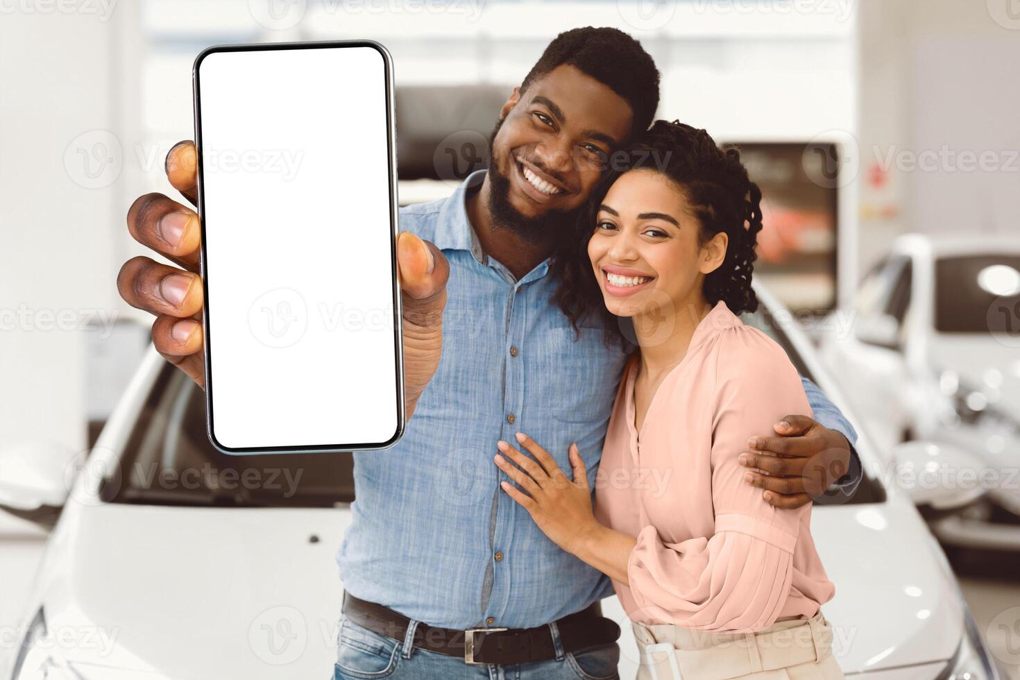 Car Buyers. African Spouses Showing New Vehicle Key To Camera Smiling And Hugging Near Auto In Dealership Showroom. photo