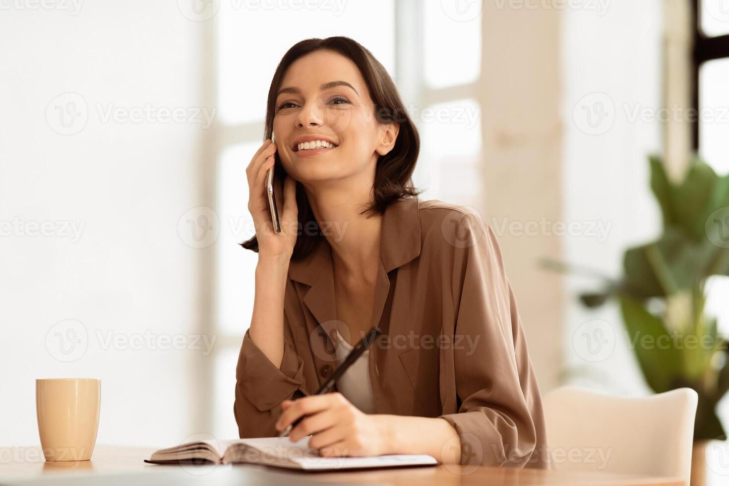 Corporate Communication. Happy female manager talking on mobile phone and writing memo in her hotebook, copyspace photo