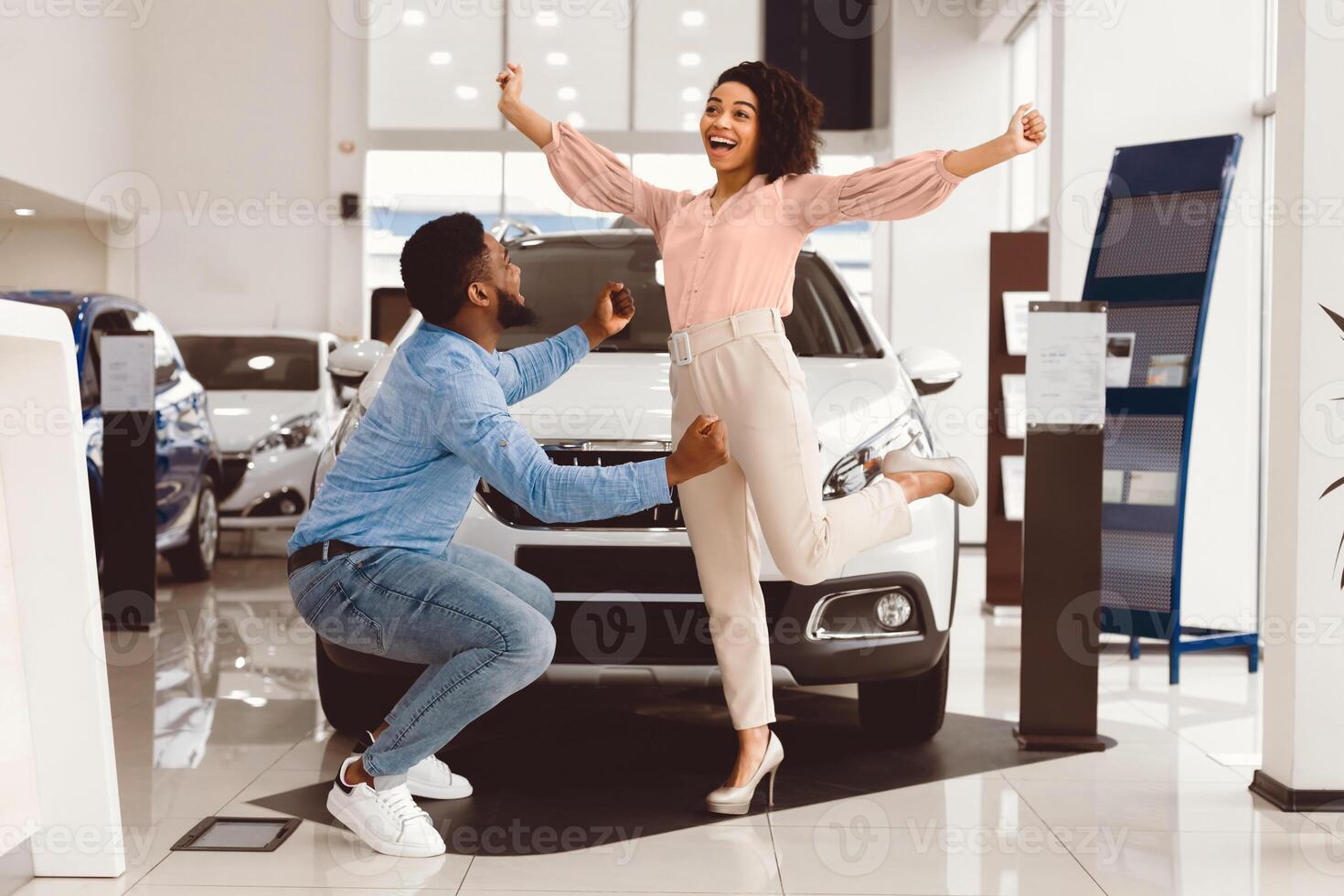New Family Car. Automobile Buyers Spouses Celebrating Buying Auto Jumping In Joy And Shaking Fists In Dealership Store photo