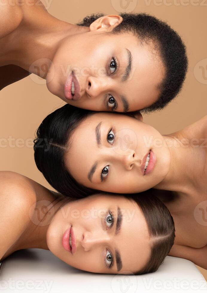 Female Beauty. Portrait Of Three Attractive Women Models With Perfect Soft Face Skin Looking At Camera Over Beige Studio Background photo