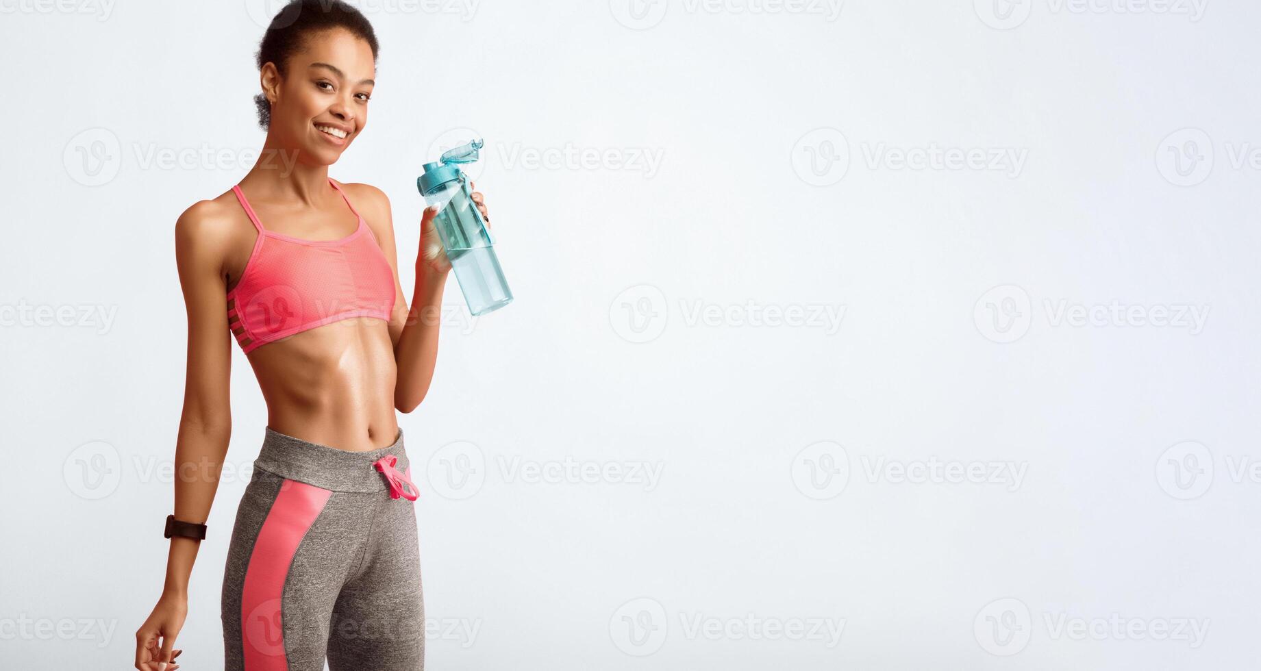Hydration. Slim Afro Girl Holding Water Bottle Smiling At Camera Posing Over Pink Studio Background. Empty Space photo
