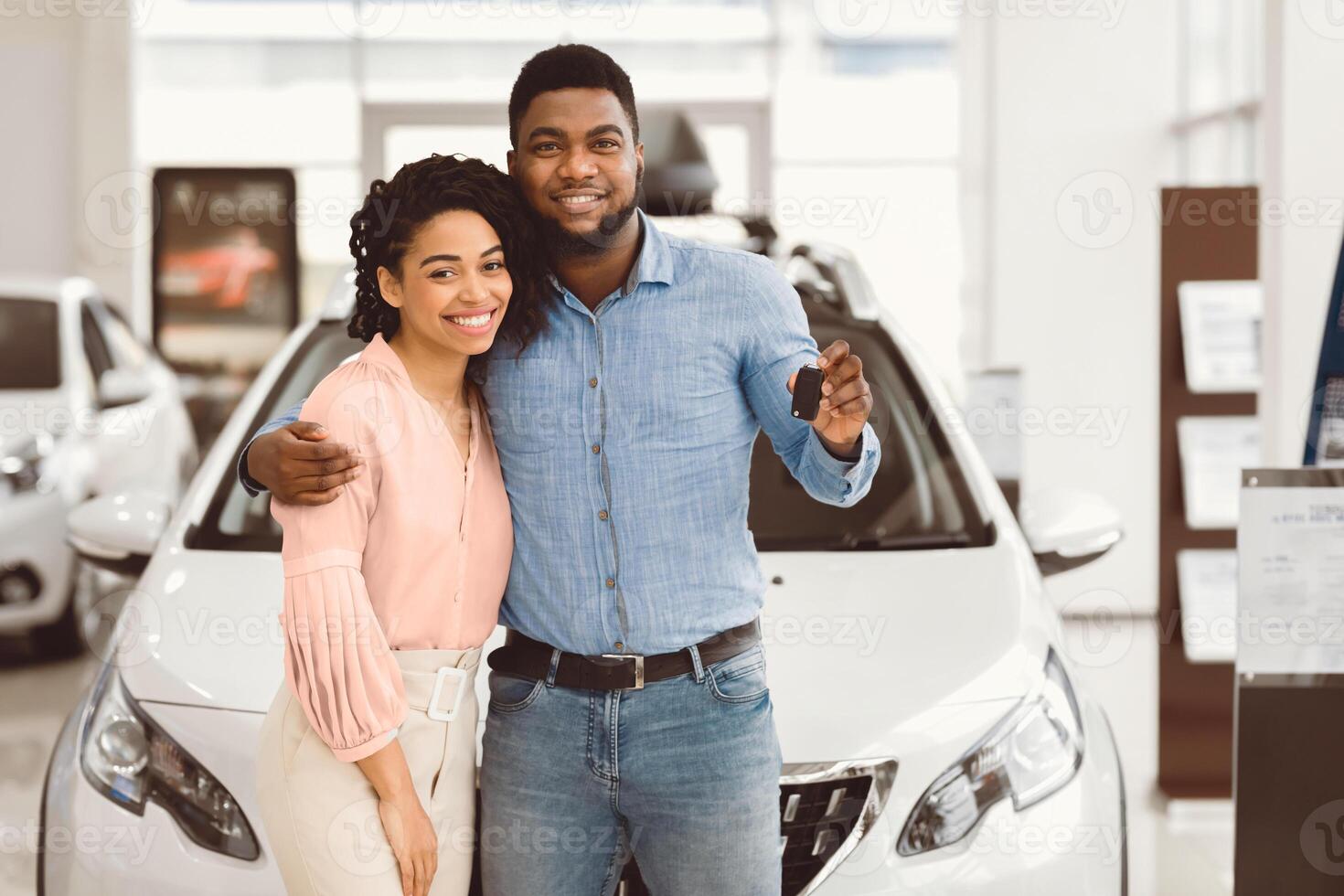 Joyful Black Couple Holding New Car Key Smiling At Camera Posing Standing Near Luxury Auto In Dealership Store photo