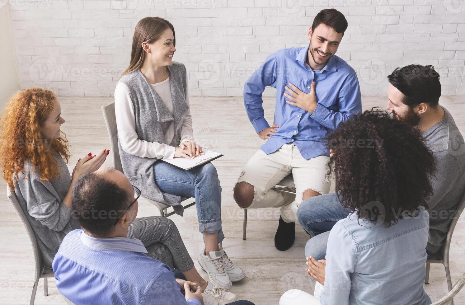 Cheerful man appreciates support of people at rehab group meeting, empty space photo