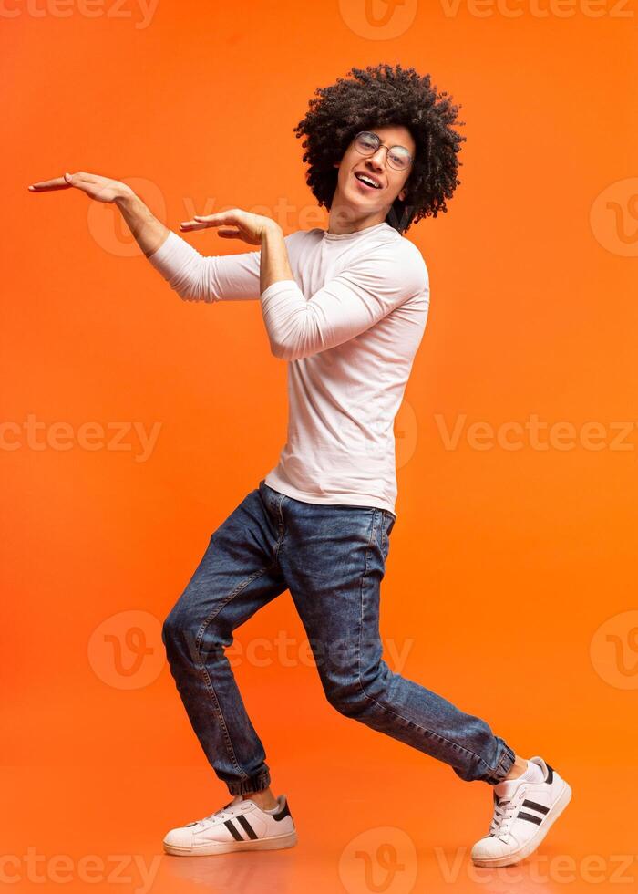 Funny black guy fooling, dancing in egypt style on orange studio background photo