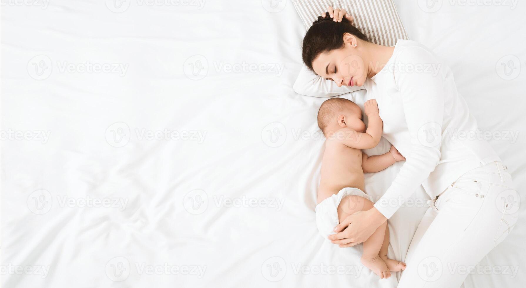 Sweetest dream with baby. Mother embracing her napping baby in bed, sleeping together, top view with empty space photo