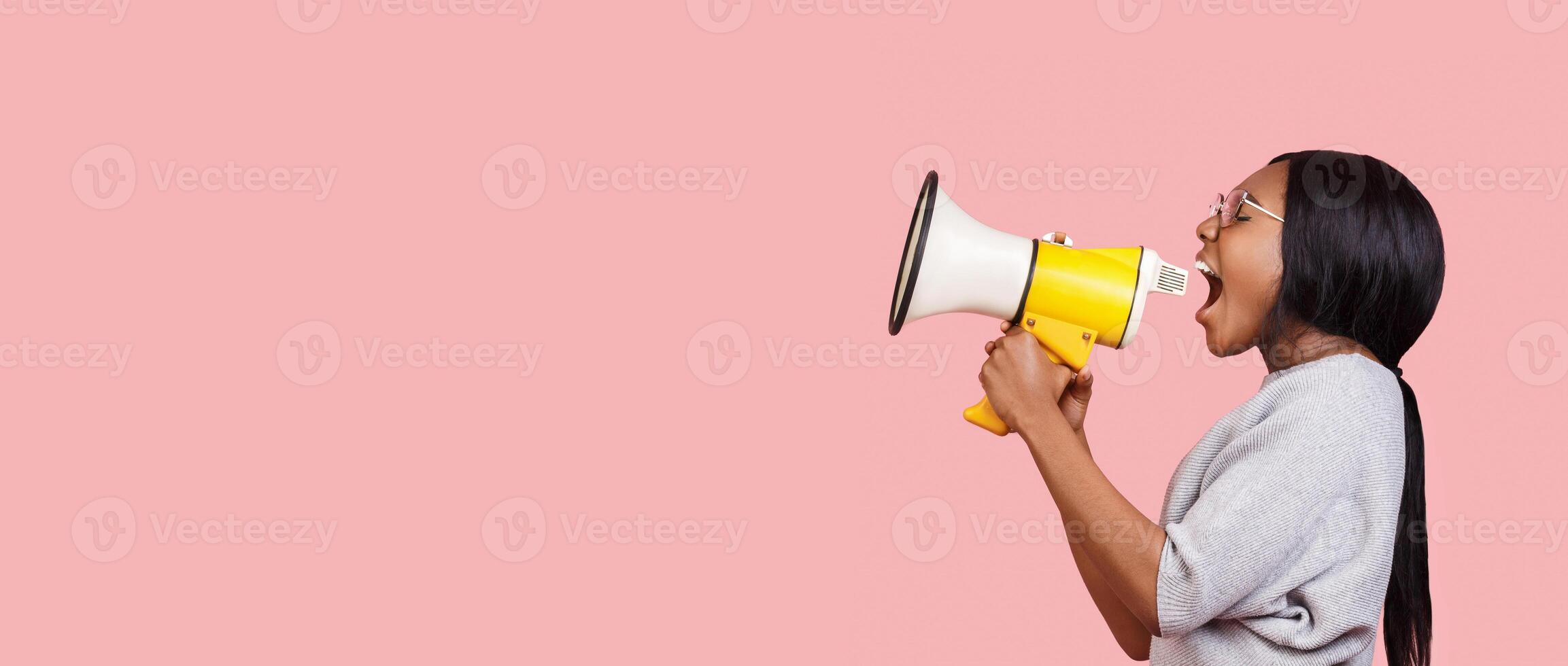 Making announcement. Black woman shouting in megaphone towards copy space over pink background, panorama photo