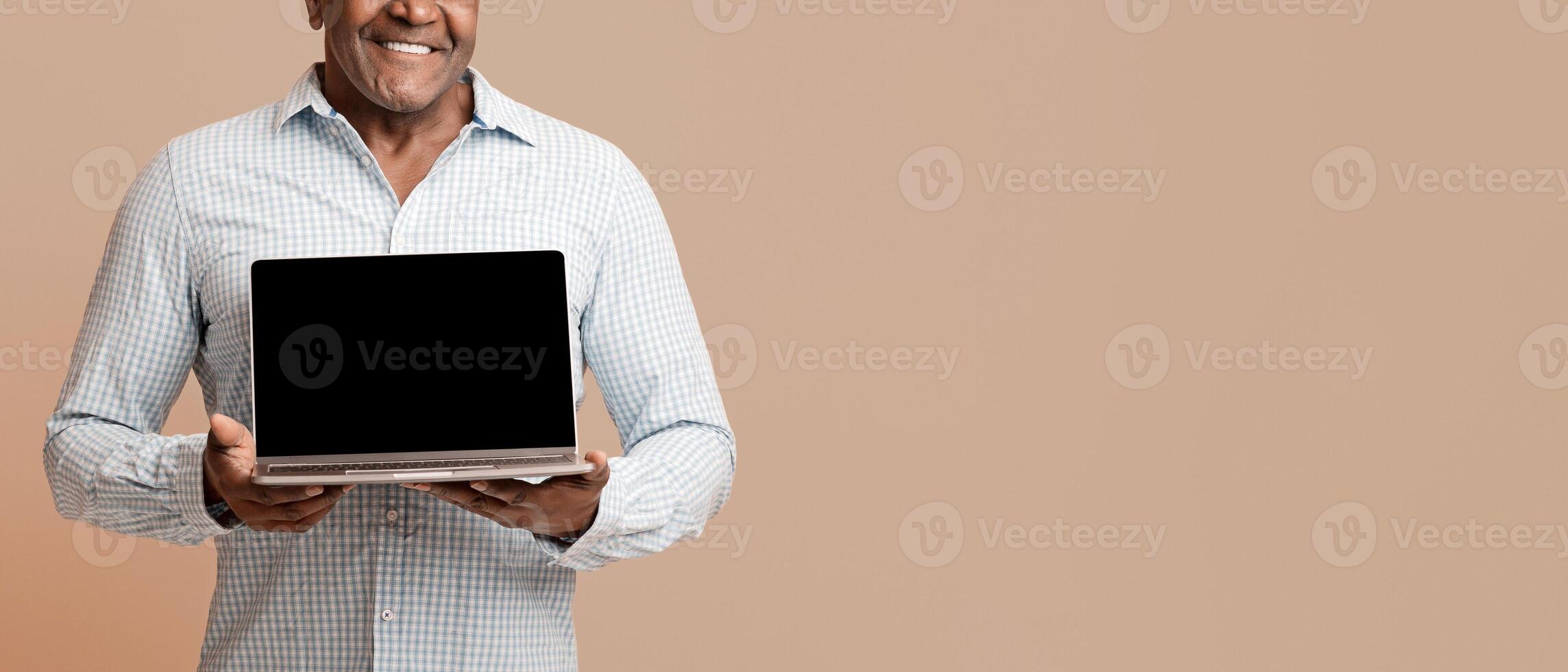 Modern lifestyle for old people. Mature african man showing blank screen of laptop, orange studio background photo