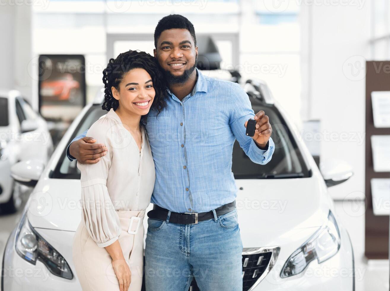 Joyful Black Couple Holding New Car Key Smiling At Camera Posing Standing Near Luxury Auto In Dealership Store photo