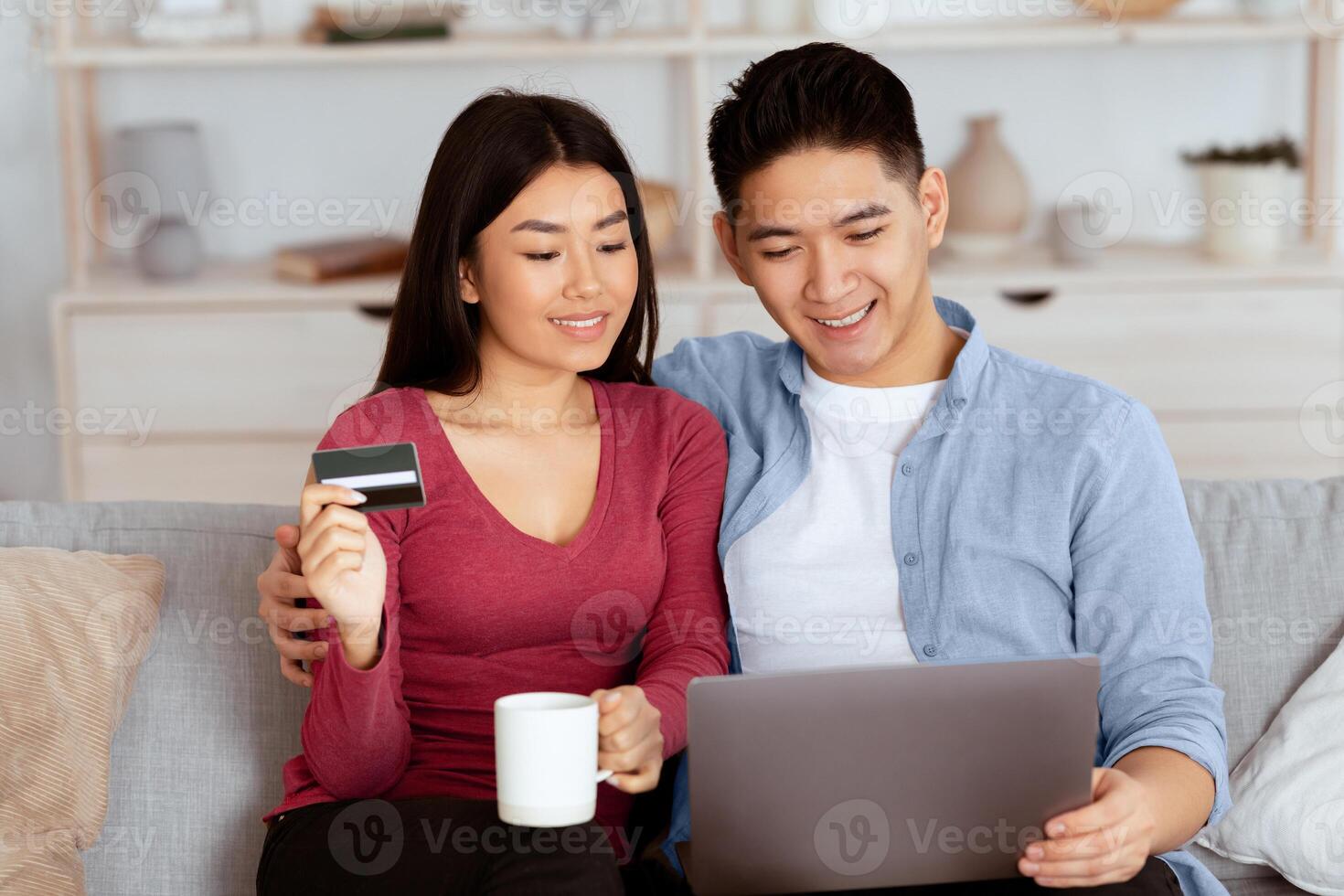Online Shopping. Chinese couple using laptop computer and credit card sitting on couch at home on weekend photo