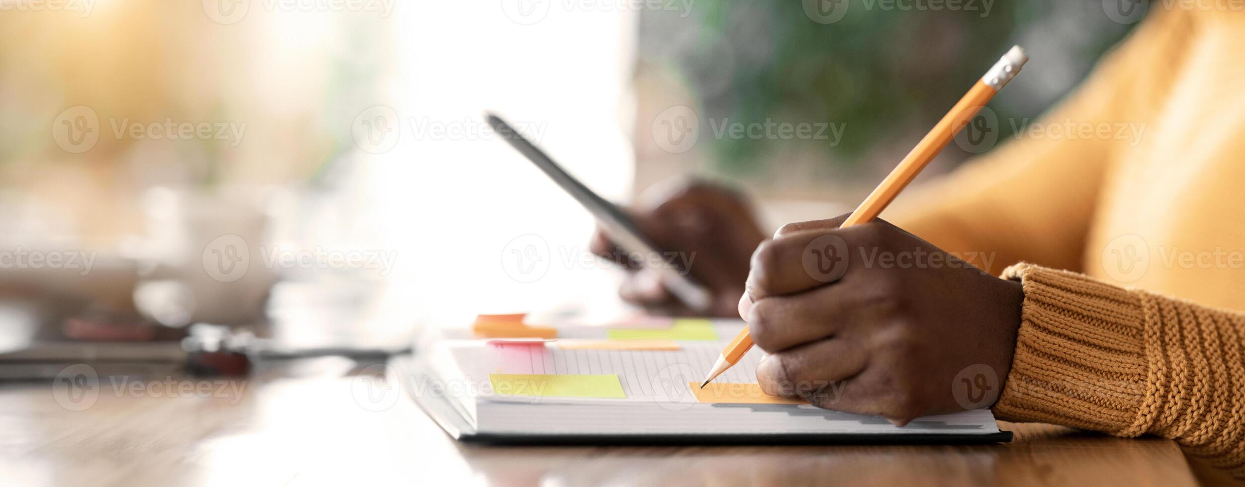 Day-planning concept. Cropped of afro woman organising her day, looking at smartphone and taking notes at notepad, cafe interior photo