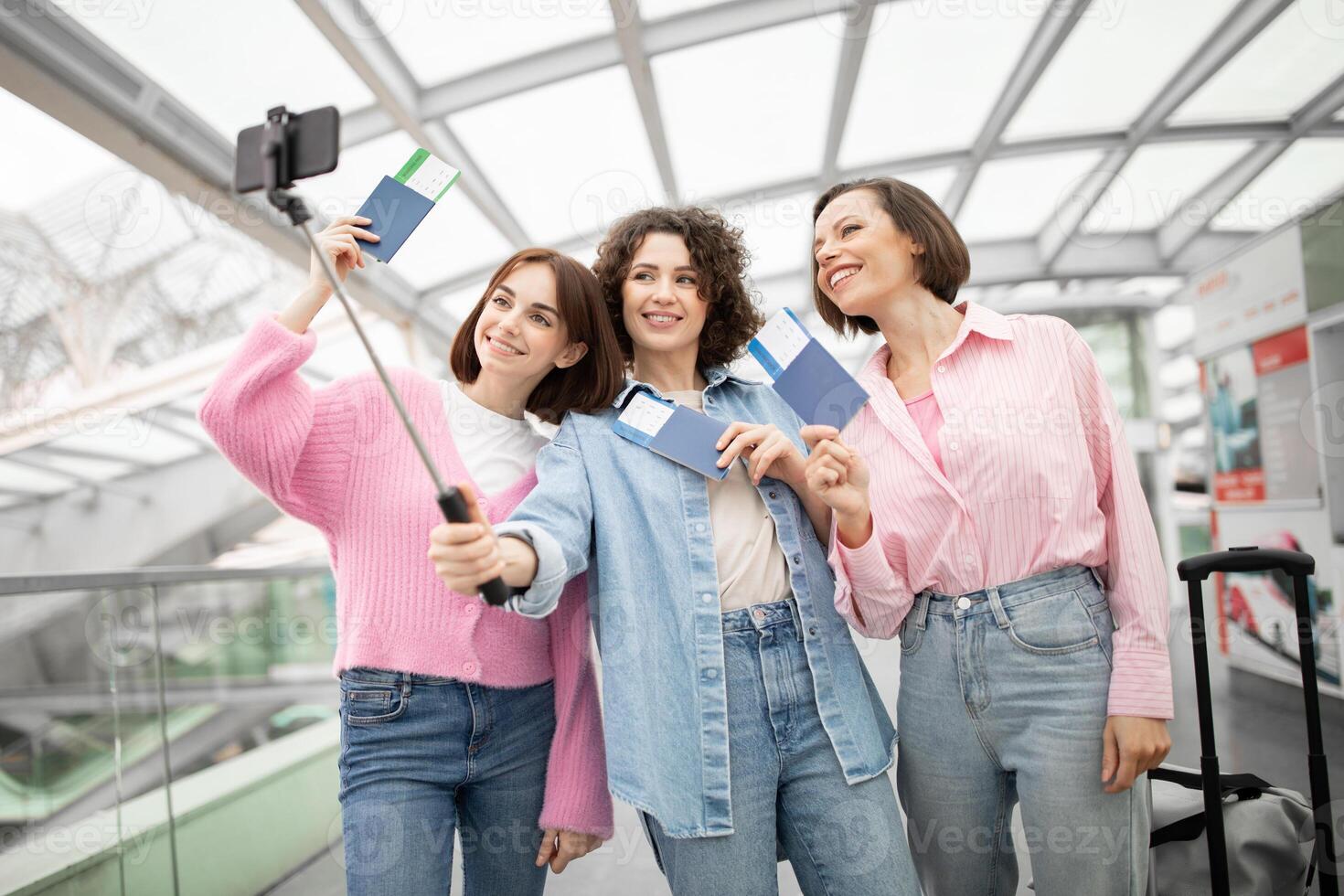 Three friends enjoy a lighthearted moment at the airport, capturing a selfie while holding their boarding passes. They are excited for their upcoming journey together. photo