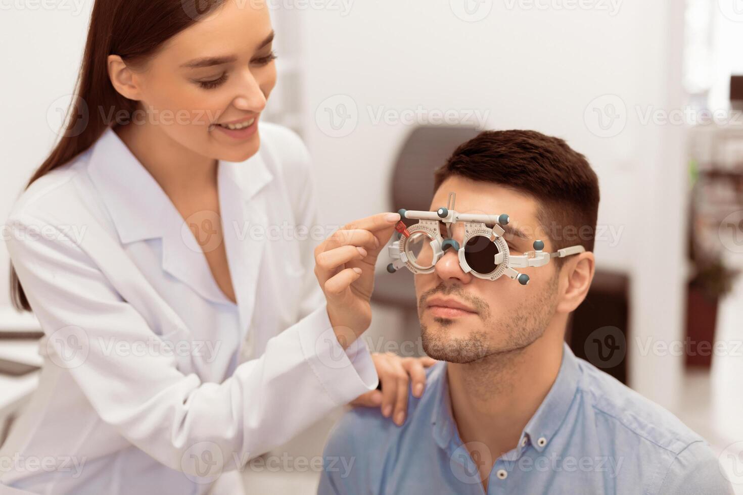 Eyesight Test Concept. Beautiful lady optometrist checking patient's vision with trial frame, one eye closed photo