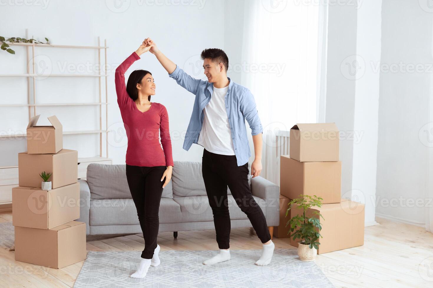 Celebrating Moving Day. Happy young asian tenants dancing among unpacked boxes in new home photo