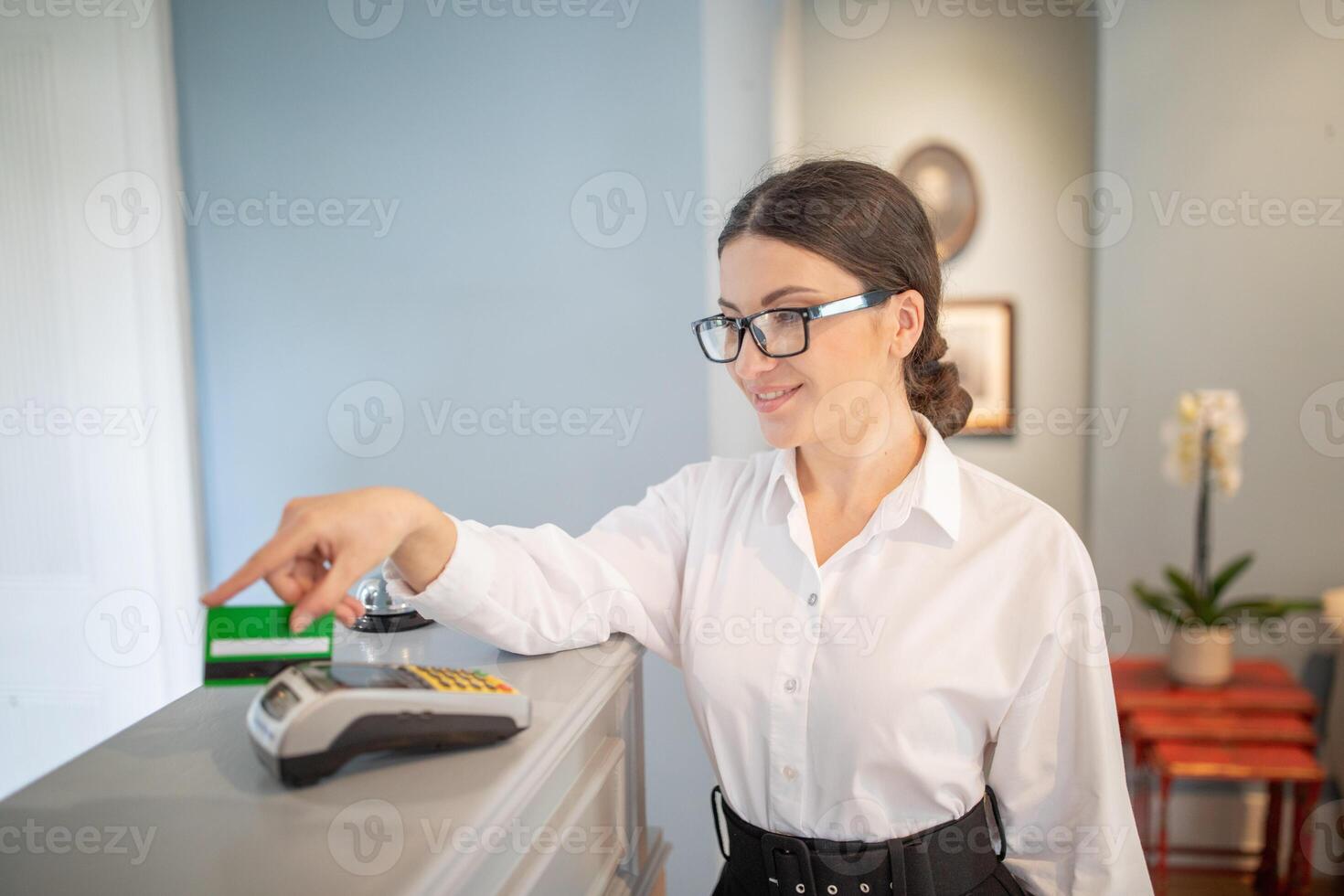A young woman in glasses guides a customer through the payment process at a contemporary retail shop. Her friendly demeanor enhances the shopping experience, creating a welcoming atmosphere. photo