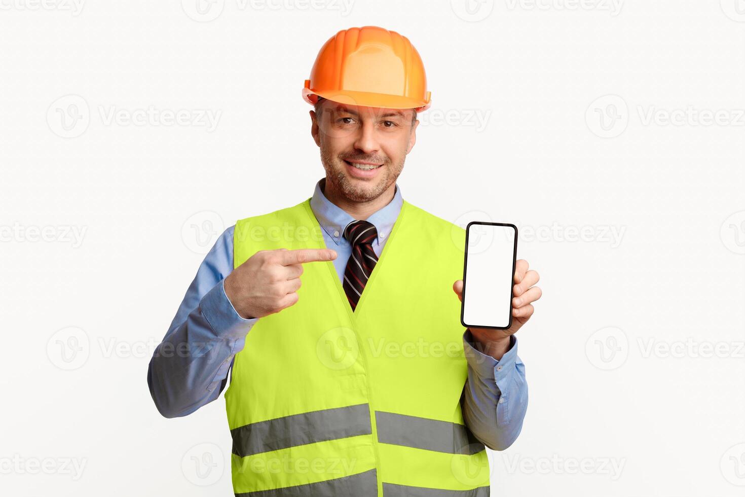 Construction Worker Showing Smartphone Blank Screen, Pointing Finger Recommending Building Services Standing In Studio On White Background. Mockup photo