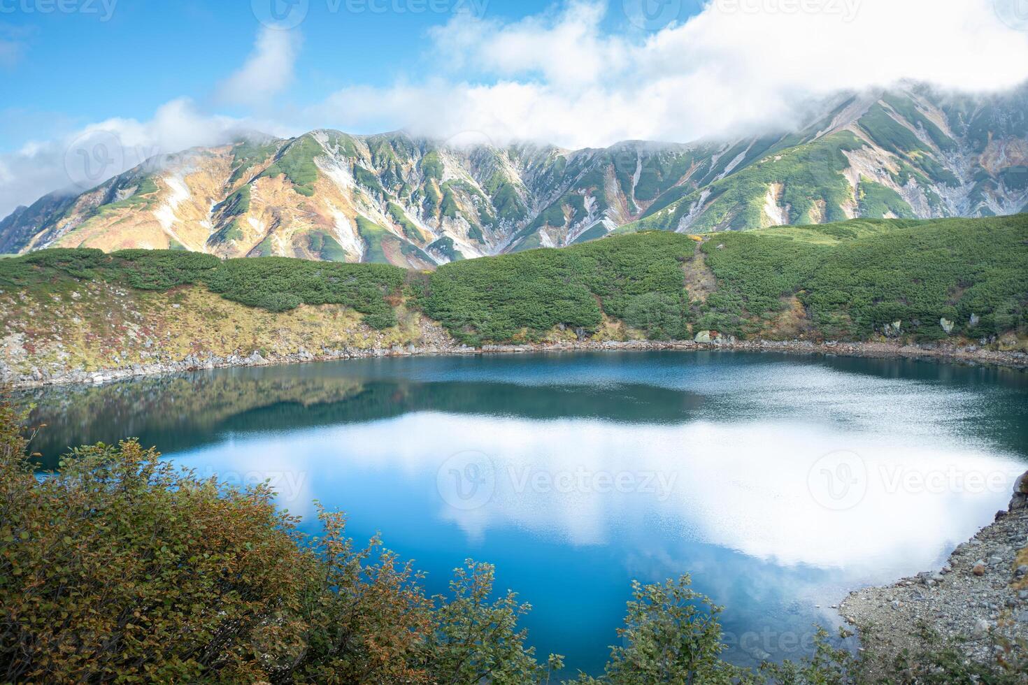 Murodo, Tateyama Kurobe Alpine Route, Japan, A stunning landscape featuring a serene lake surrounded by lush greenery and majestic mountains under a partly cloudy sky. photo