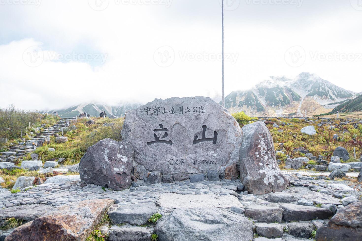 Murodo, Tateyama Kurobe Alpine Route, Japan, A stone monument with text Chubu Sangaku National Park Tateyama Murododaira 2450 in Japanese, a mountainous trail, surrounded by lush greenery photo