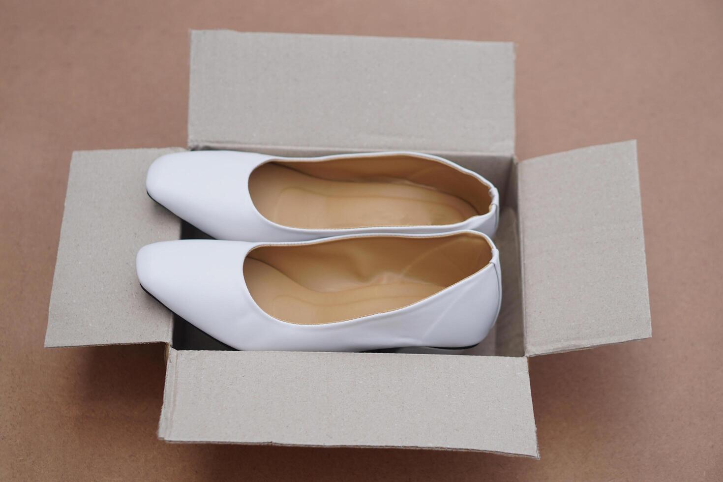 White shoes in brown cardboard box from shopping online or shoe shops. Concept, fashion, formal and polite footwears to match with white uniform or outfit. New shoes. photo