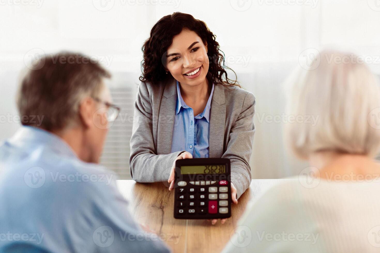 Senior couple receiving financial advice from mexican insurance consultant who showing them calculator photo