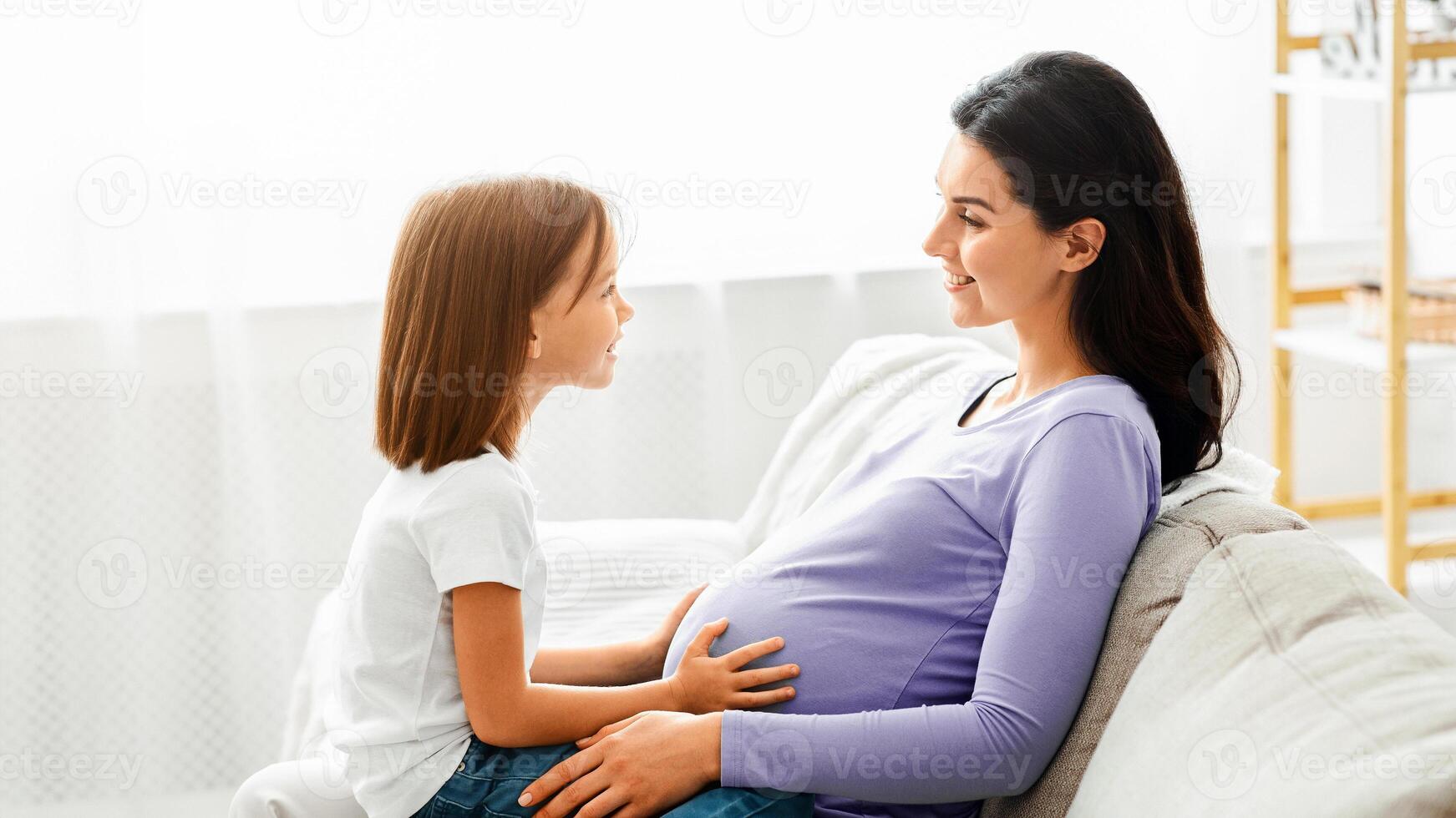Expecting mother having conversation with her little preschool daughter, spending time together at home photo