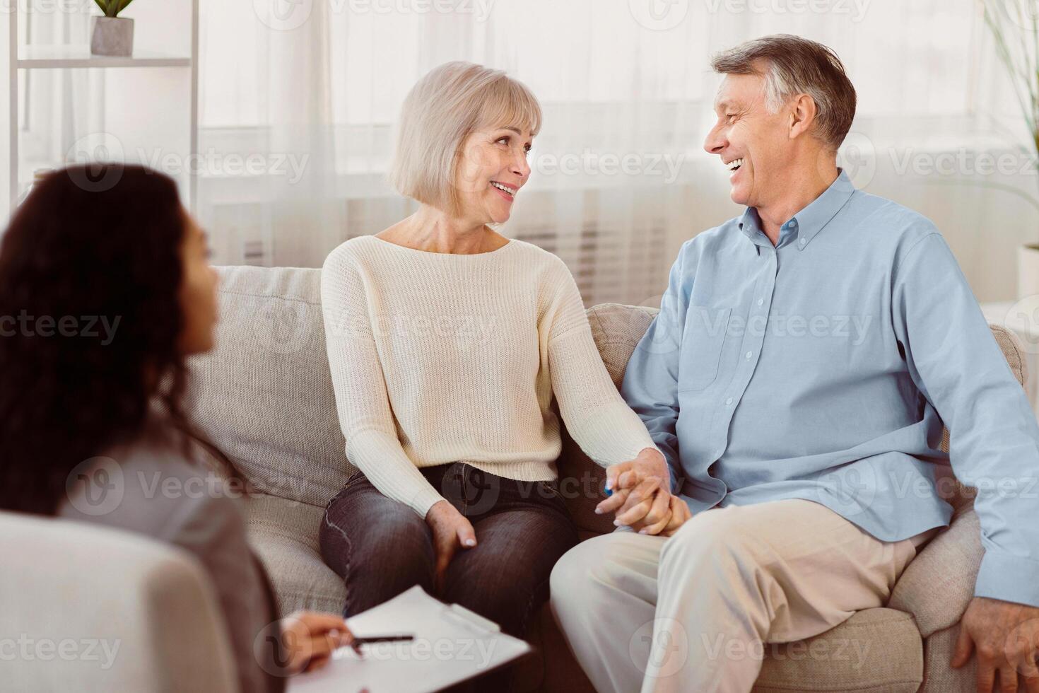 Love And Family Concept. Happy mature couple holding hands, looking at each other at psychologist office after session photo