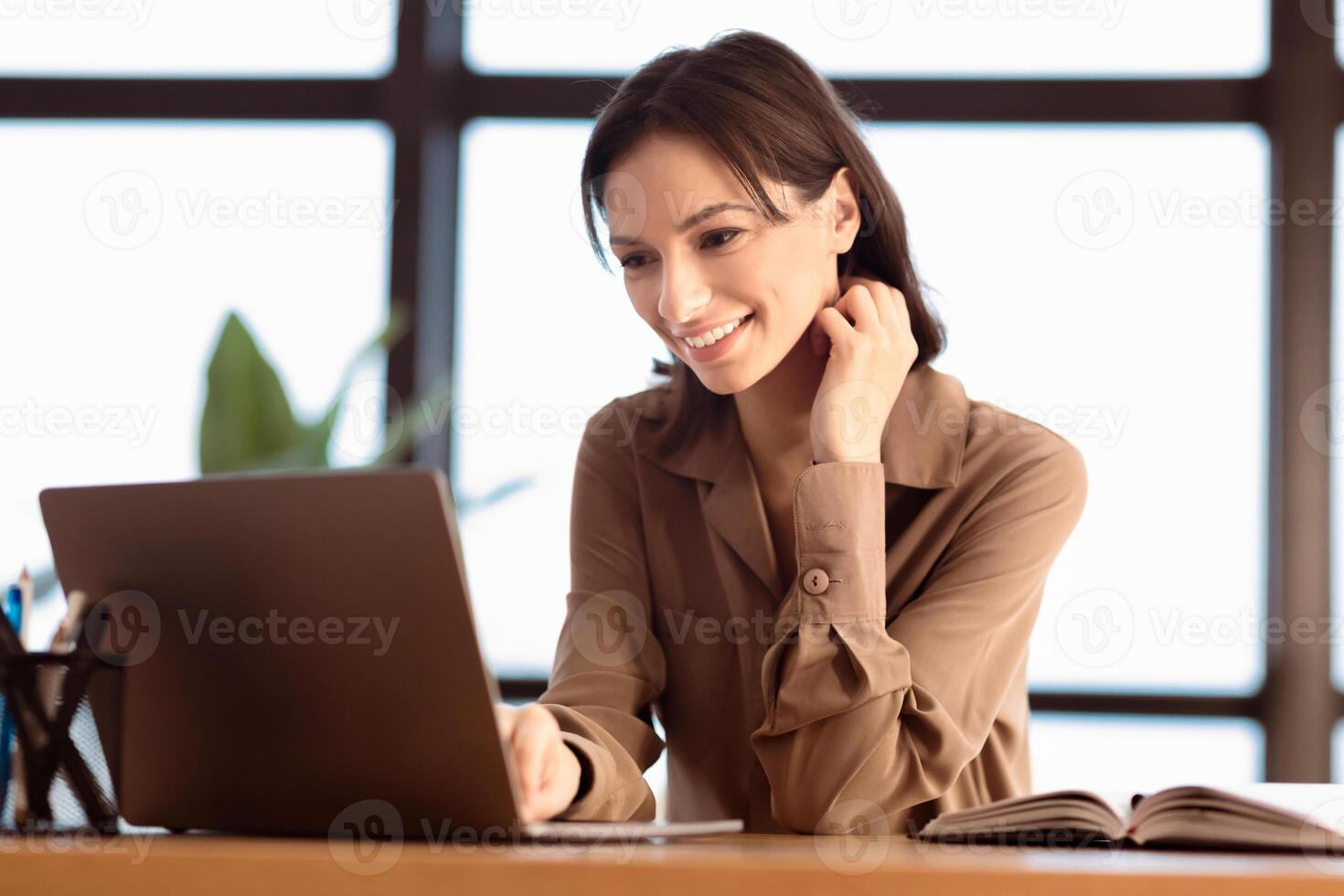 Online Education. Smiling caucasian girl studying on computer in modern office, sitting at desk by window, free space photo