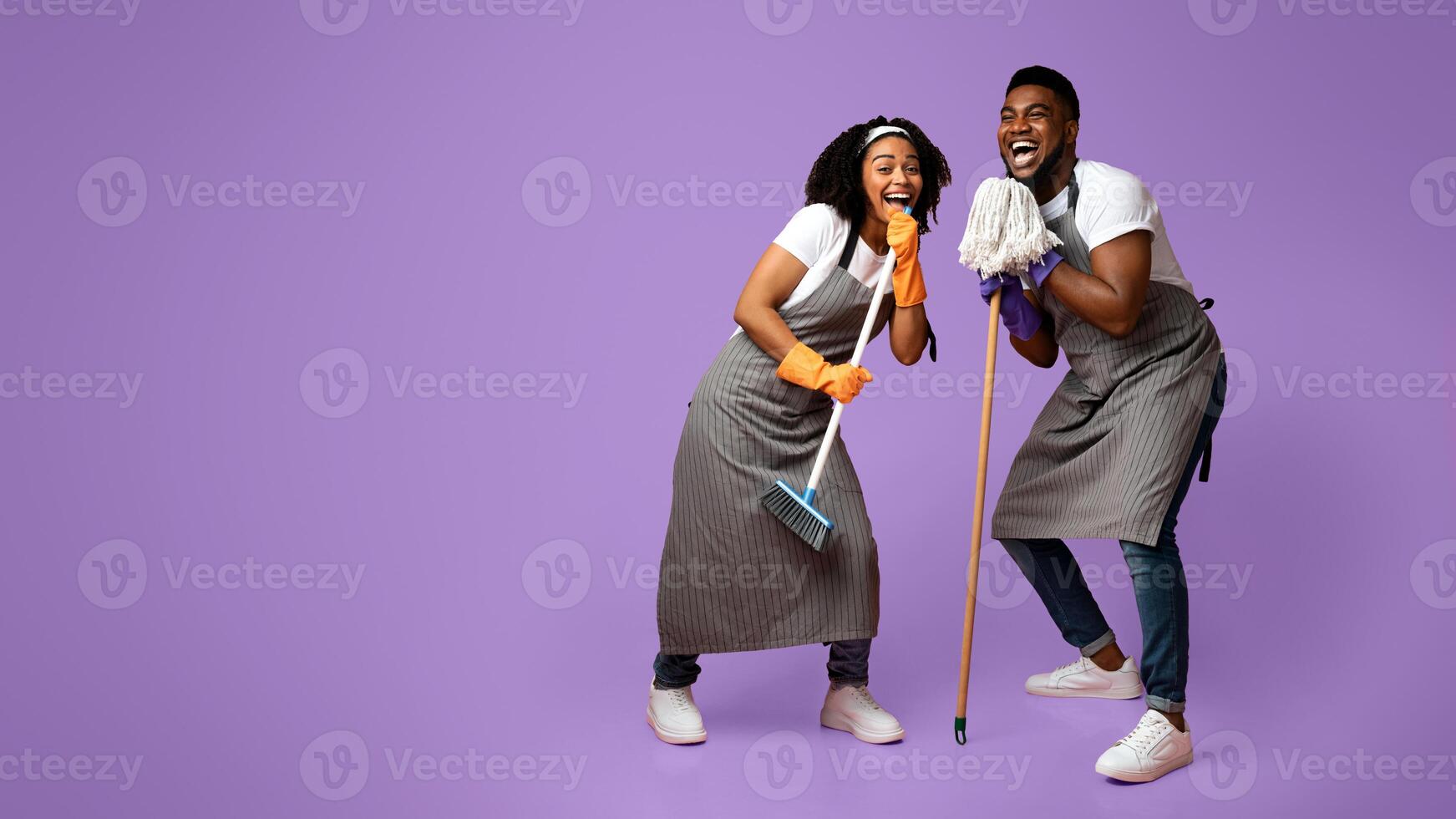 Domestic Band. Happy Black Couple Fooling Together While Cleaning Flat, Singing Into Mop And Broom, Standing On Pink Background In Studio, Free Space photo