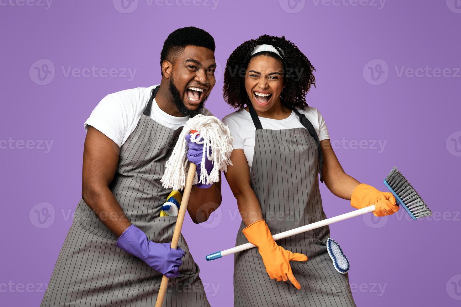 Cleaning Fun. Playful Black Couple Using Mop As Microphones, Having Fun During Tidying, Singing Together Over Pink Background, Copy Space photo