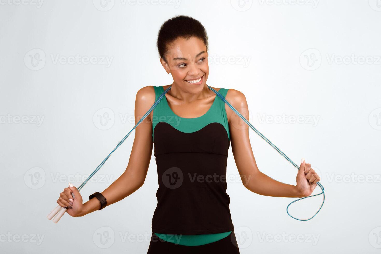 Sport Lifestyle. Playful Afro Girl Holding Jump Rope Smiling Bititng Lips Standing On Yellow Background. Studio Shot photo