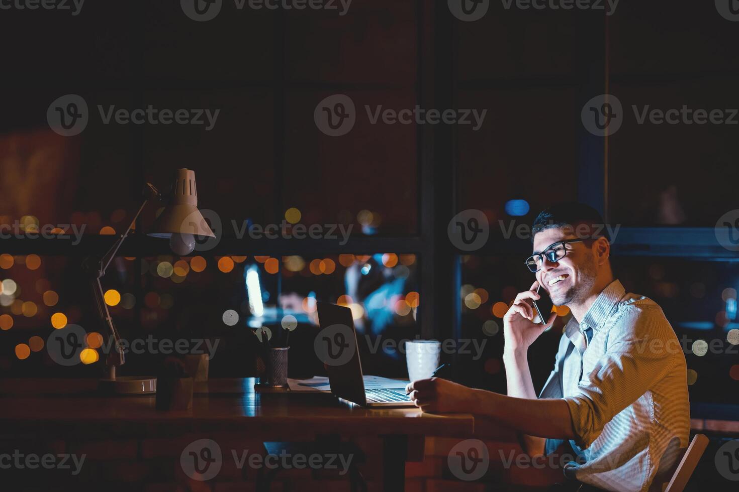 Successful Businessman Talking On Phone Working Sitting Near Window In Modern Office At Night. Copy Space photo