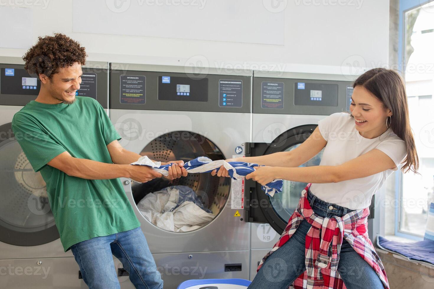 A man and woman engage in a fun tug-of-war with laundry while doing their chores at a laundromat, creating a lively atmosphere in the shared space. photo