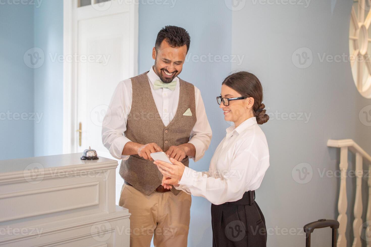 A smiling hotel receptionist assists a guest with their check-in process at an inviting boutique hotel during the day, showcasing a warm hospitality experience. photo