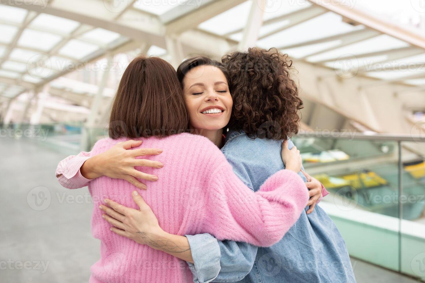 Three friends share a warm hug in a contemporary indoor space, expressing their joy and connection. The ambiance highlights their happiness and friendship in a stylish, airy setting. photo