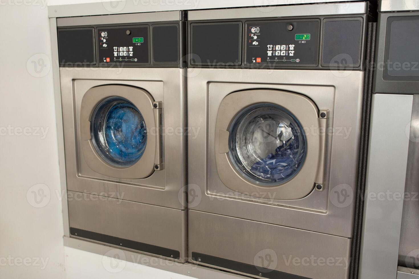 Two stainless steel washing machines in a bright, modern laundromat display their tumbling laundry. The area is well-lit, creating a welcoming atmosphere for customers. photo